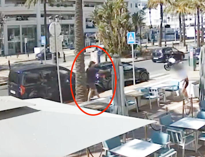 Flagrante de câmera de segurança mostra um homem armado abordando uma vítima na calçada de Marbella durante o dia, capturado em imagem de alta definição, com detalhe de círculo vermelho destacando o agressor.
